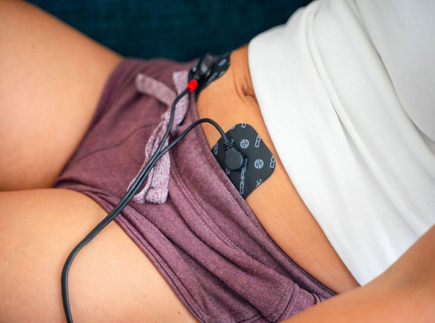 Une femme qui utilise l'électrostimulation sur son ventre pour soulager ses règles douloureuses