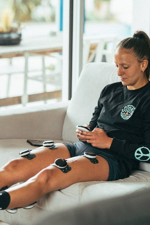 A woman using the Compex SP 8.0 EMS muscle stimulator for a calf and quad muscle recovery session