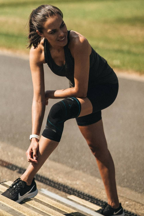A woman stretching wearing the Compex Activ' Knee+