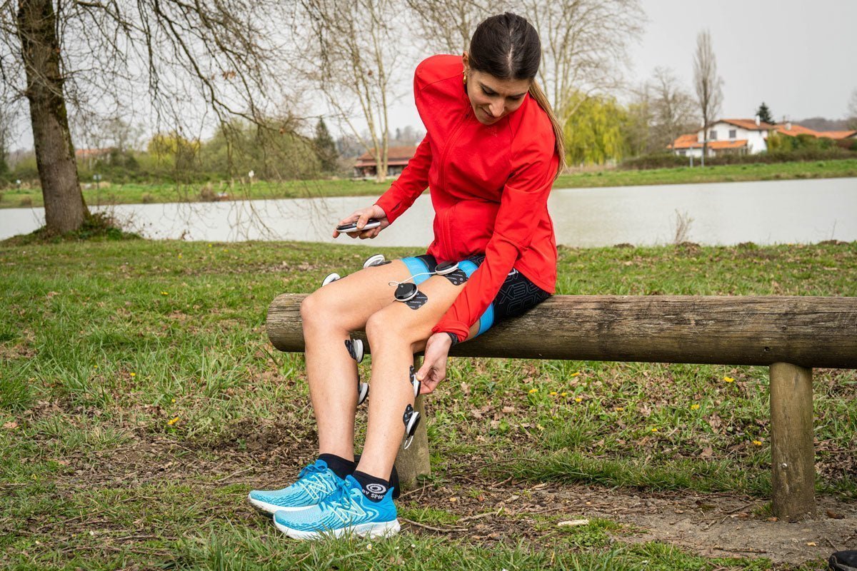 Une personne qui utilise l'électrostimulation Compex sur ses mollets pour mieux récupérer