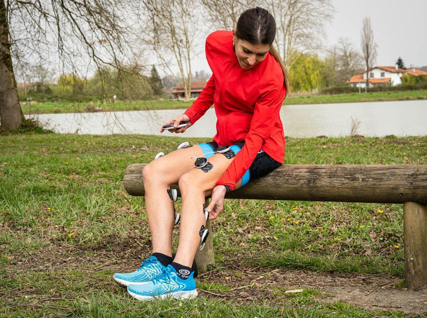 Une personne qui utilise l'électrostimulation Compex sur ses mollets pour mieux récupérer
