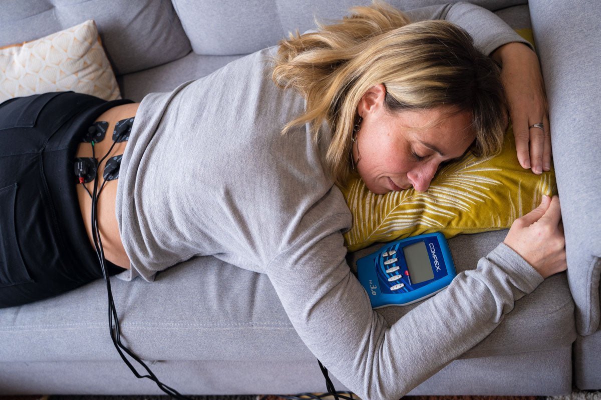 Une femme qui utilise l'électrostimulation Compex pour soulager son lumbago