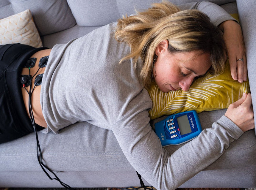 Une femme qui a les électrodes Compex dans son bas du dos pour soulager son dos avec l'électrostimulation