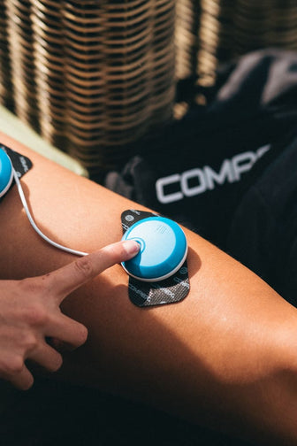 A woman turning on the module of her Compex FIT 5.0 EMS muscle stimulator