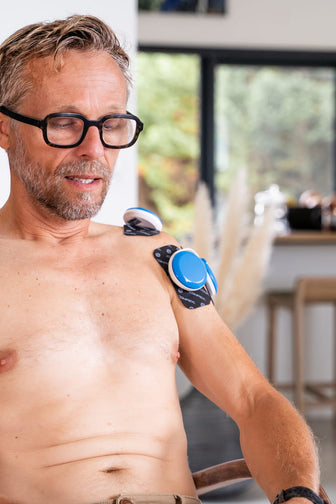 A man adjusting the Compex FIT 5.0 EMS muscle stimulator to do some rehabilitation on his shoulder