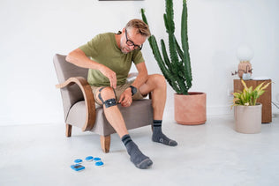A man placing black Compex electrodes on his knee