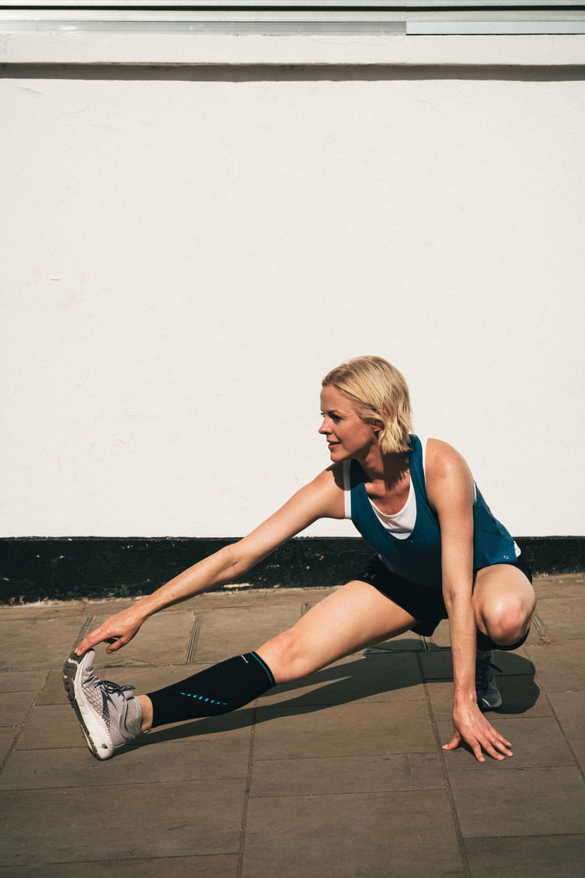 A woman stretching while wearing the Compex Activ'® calf sleeves