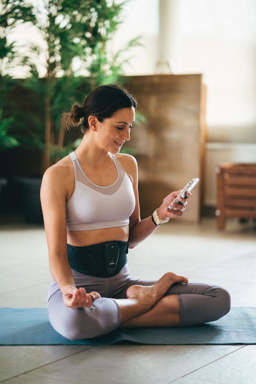 A woman using the Compex Corebelt EMS muscle stimulator belt