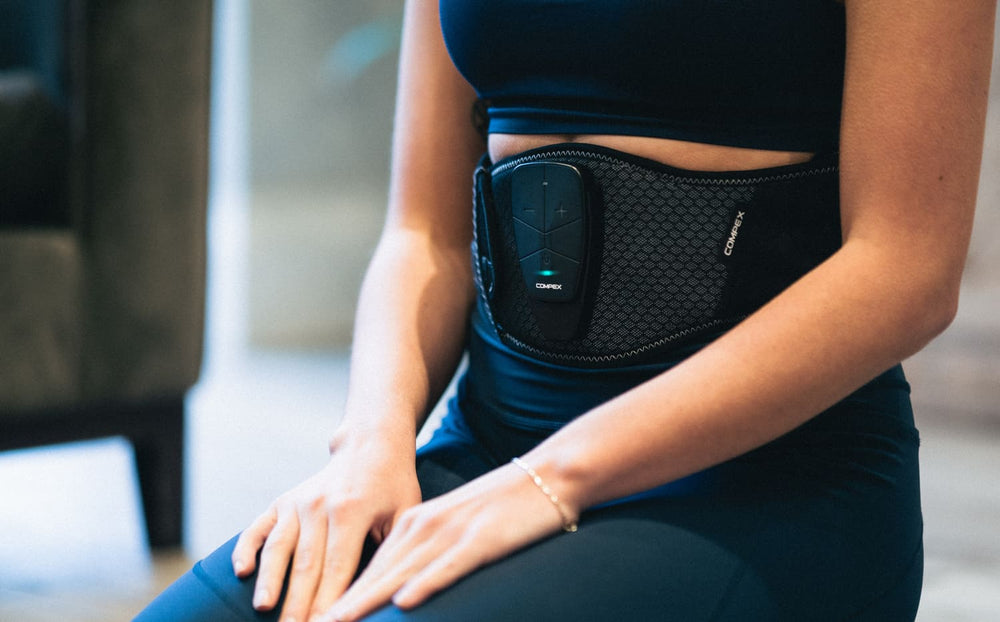 A woman using the Compex Corebelt 3.0 EMS muscle stimulator belt