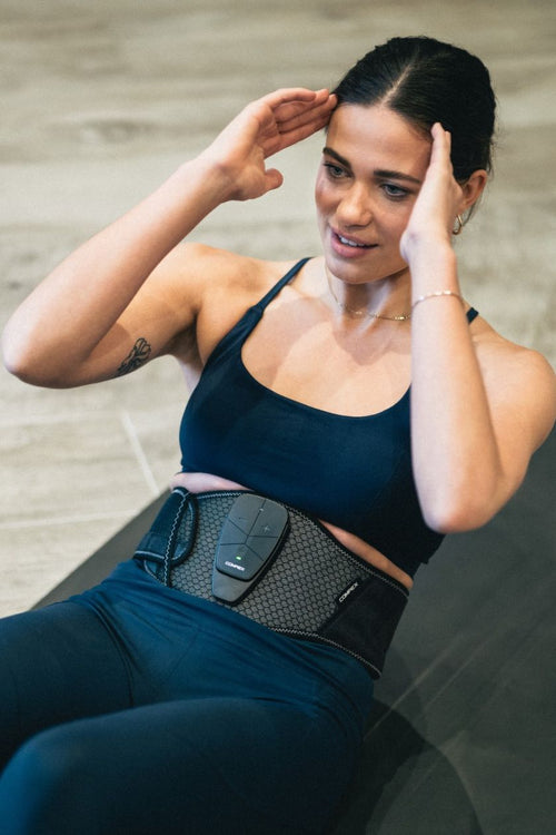 A woman doing a crunch using the Compex Corebelt 3.0 EMS muscle stimulator belt