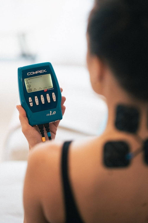A woman using the Compex FIT 1.0 EMS muscle stimulator for a neck massage session