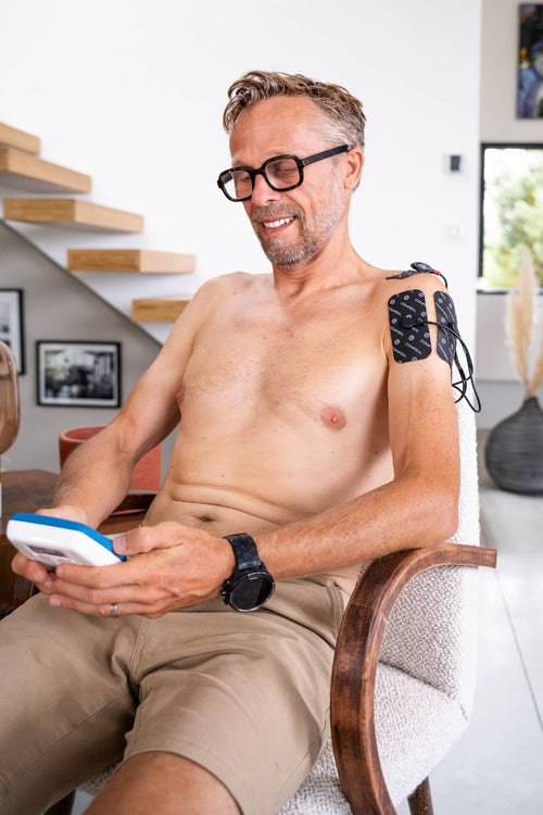 A man using the Compex FIT 1.0 EMS muscle stimulator for a shoulder pain relief session