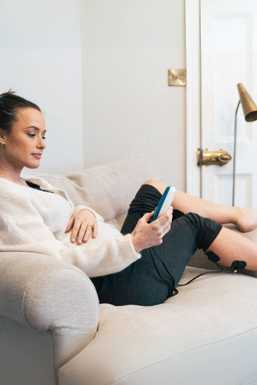 A woman using the Compex FIT 1.0 EMS muscle stimulator for a calf muscle recovery session