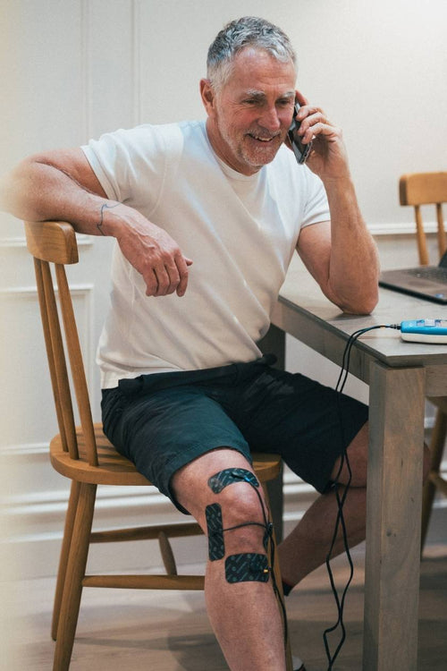 A man using the Compex FIT 3.0 EMS muscle stimulator for a knee pain relief session