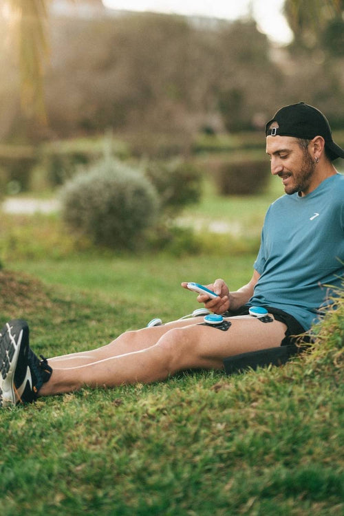 A man sitting outside using the Compex FIT 5.0 EMS muscle stimulator for a quad muscle recovery session
