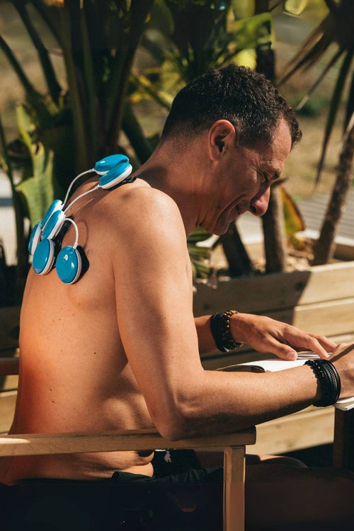 A man sitting outside using the Compex FIT 5.0 EMS muscle stimulator for a back muscle recovery session