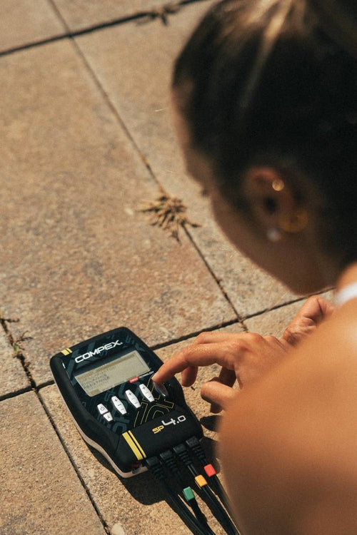 A woman using the Compex SP 4.0 EMS muscle stimulator for an ab muscle strengthening session