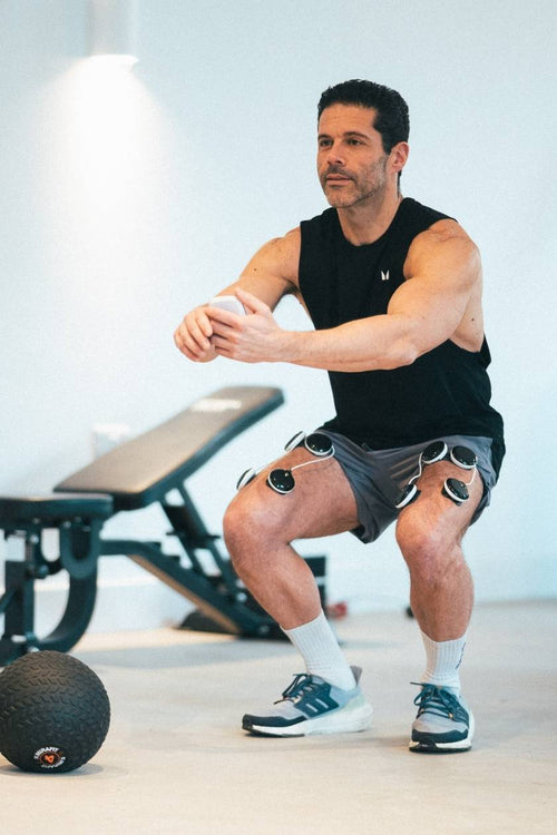 A man doing a squat, using the Compex SP 6.0 EMS muscle stimulator for a quad muscle strengthening session