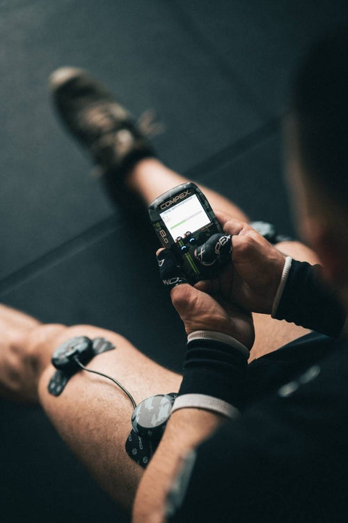 A man using the Compex SP 8.0 WOD Edition EMS muscle stimulator for a quad muscle recovery session