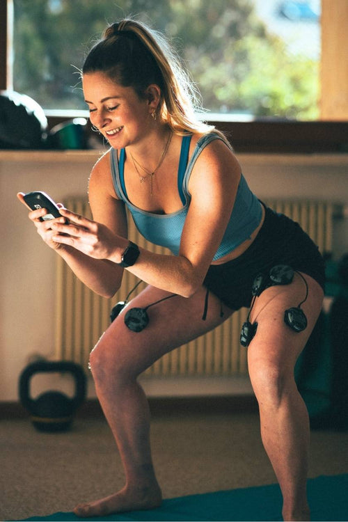 A woman using the Compex SP 8.0 WOD Edition EMS muscle stimulator for a quad muscle strengthening session