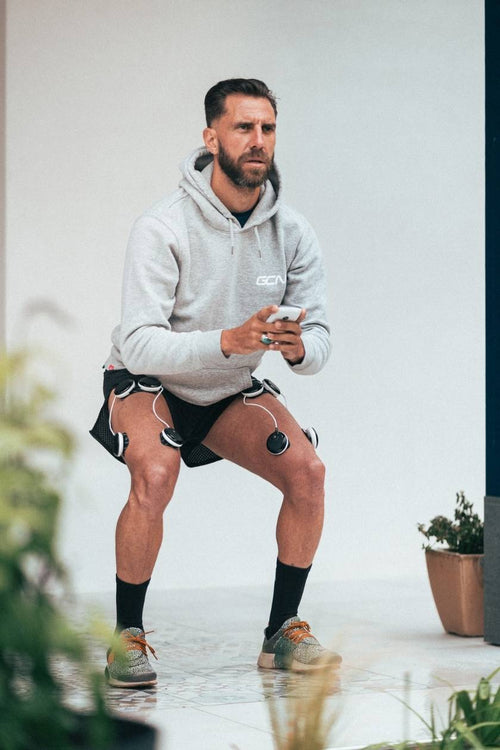 A man doing a squat, using the Compex SP 8.0 EMS muscle stimulator for a quad muscle strengthening session