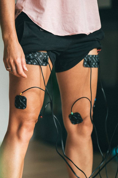 A woman using the Compex Fitness EMS muscle stimulator for a quad muscle strengthening session
