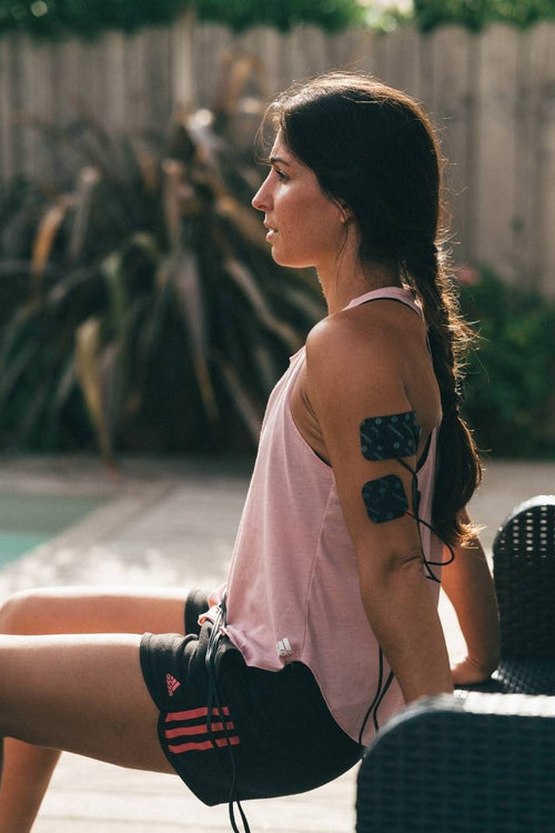 A woman using the Compex Fitness EMS muscle stimulator for a tricep muscle strengthening session