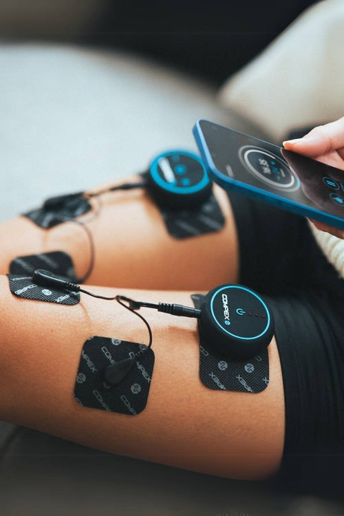 A woman sitting down using the Compex Mini EMS muscle stimulator for a quad muscle recovery session
