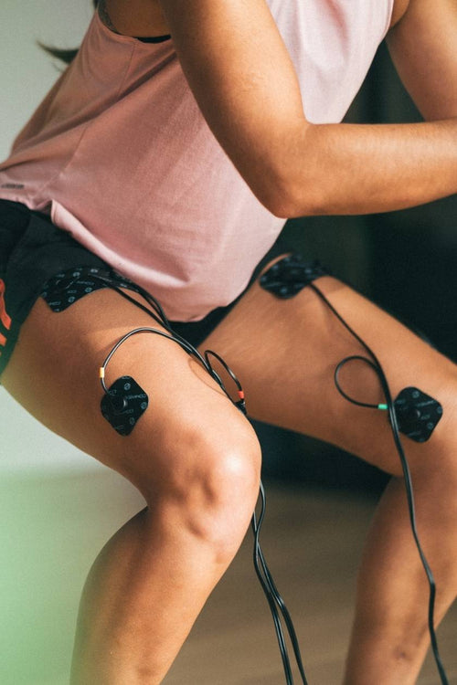 A woman doing a squat, using the Compex Sport Elite EMS muscle stimulator to strengthen her quad muscles