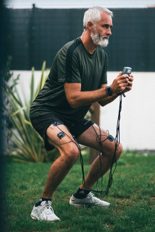 A man doing a squat, using the Compex Sport Elite EMS muscle stimulator to strengthen his quad muscles