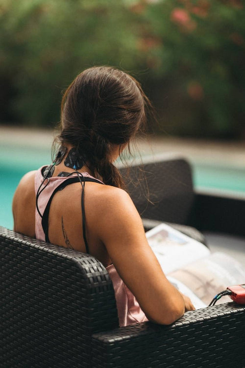 A woman using the Compex Sport EMS muscle stimulator for a neck pain relief session