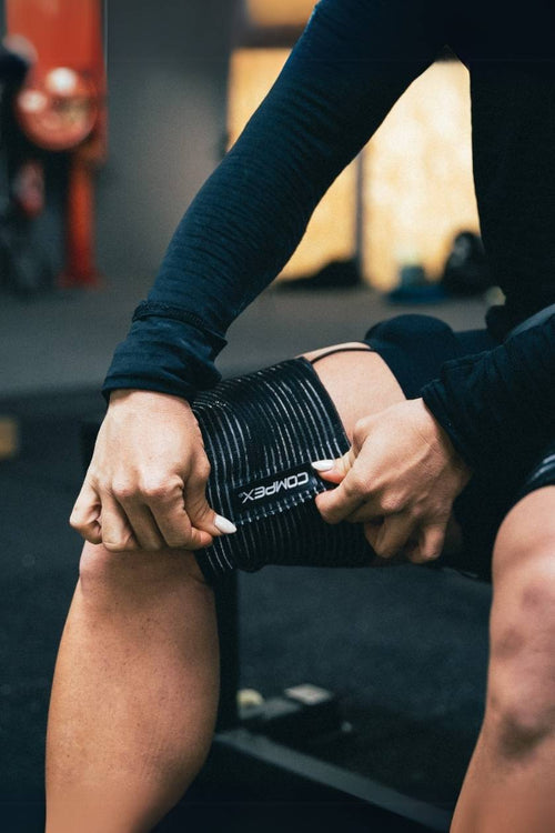 A man wrapping the Compex Elastic Straps around his quads before a strength session using the Compex SP 8.0 WOD Edition EMS Muscle Stimulator