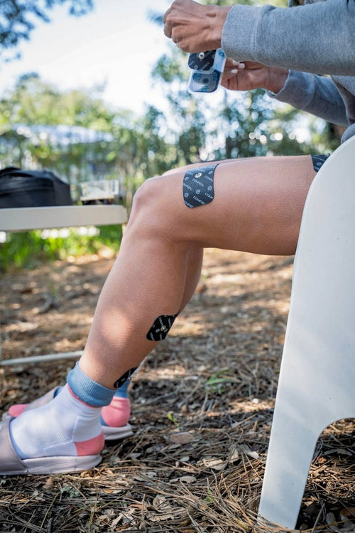 A woman placing large 1-snap Compex electrodes on her quad and calf muscles
