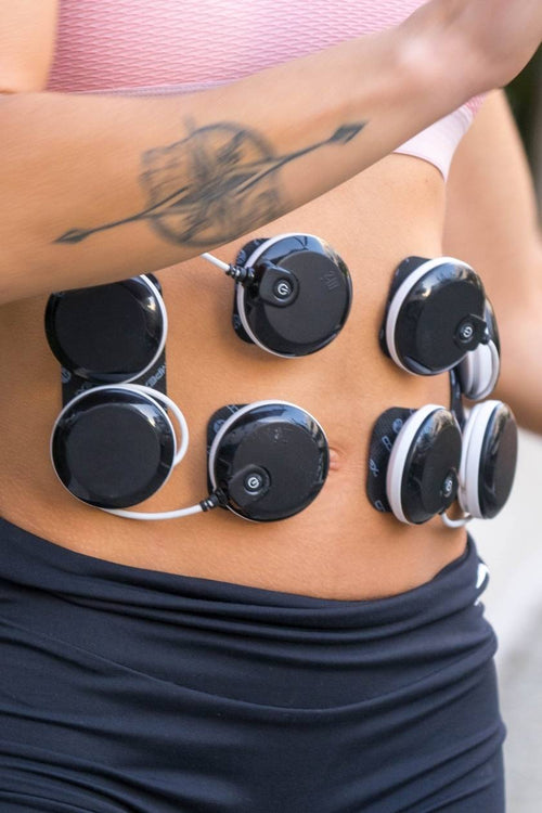 A woman using the Compex SP 8.0 EMS muscle stimulator to tone her ab muscles