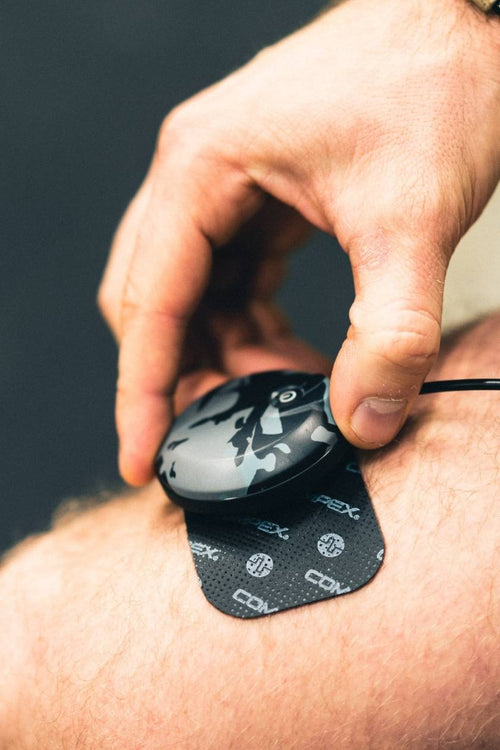 A man placing the he Compex SP 8.0 WOD Edition EMS muscle stimulator module on his quad muscles