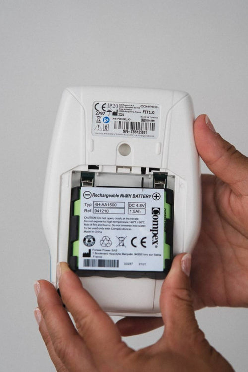 A person inserting a battery into their wired Compex EMS muscle stimulator