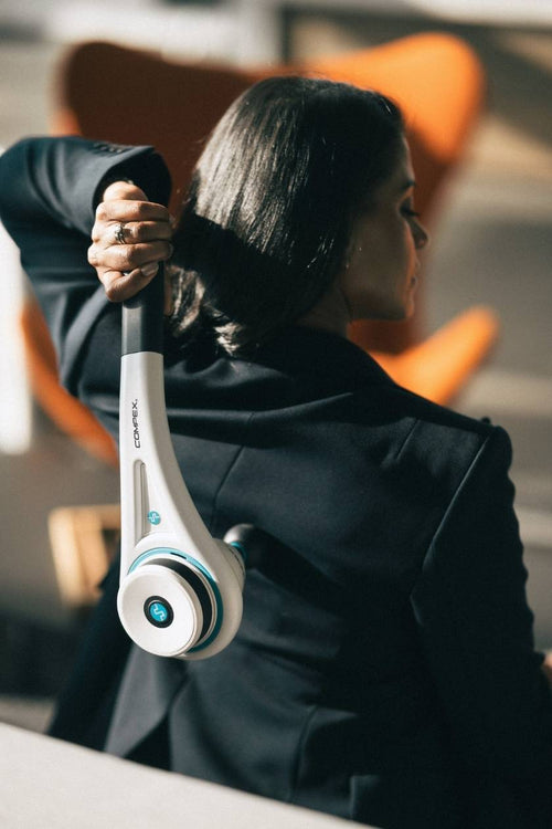 A woman sitting inside, using the Compex Fixx™ Mini massage gun for a back massage
