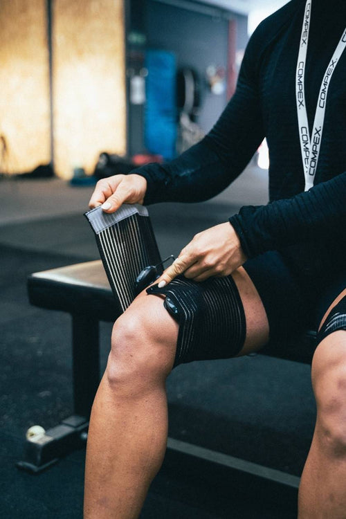 A man placing the Compex elastic straps on his quads before doing an electrical muscle stimulation (EMS) session