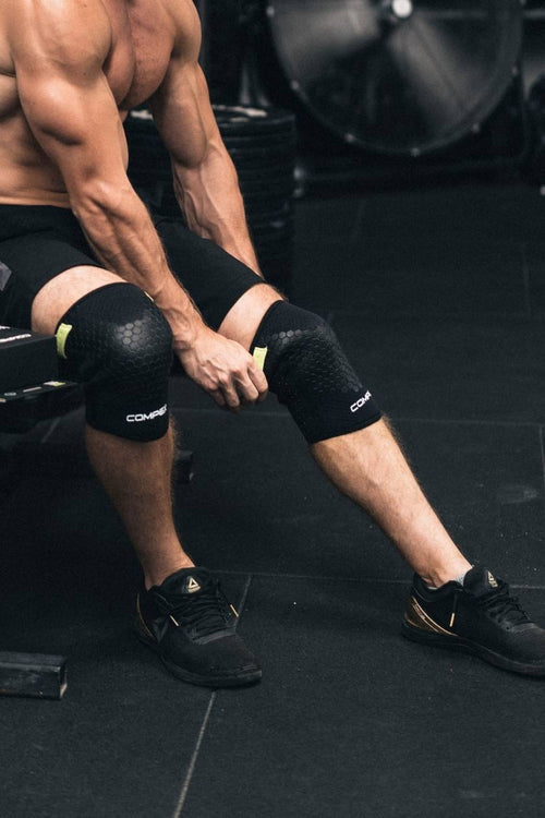 A man sitting in a gym, putting on the Compex 5mm Knee Sleeves