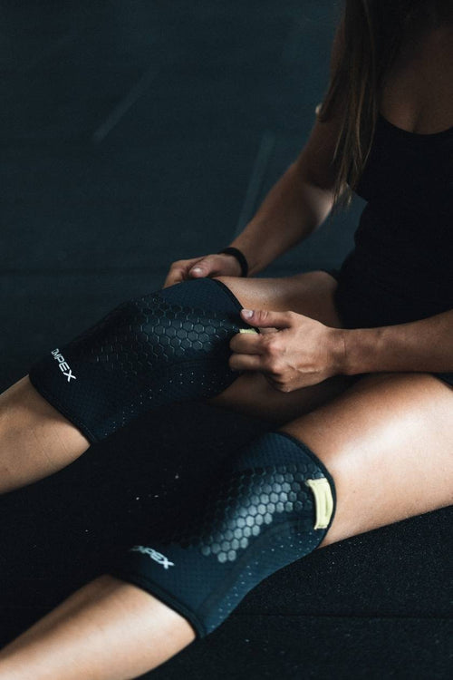 A woman sitting in a gym, putting on the Compex 5mm Knee Sleeves