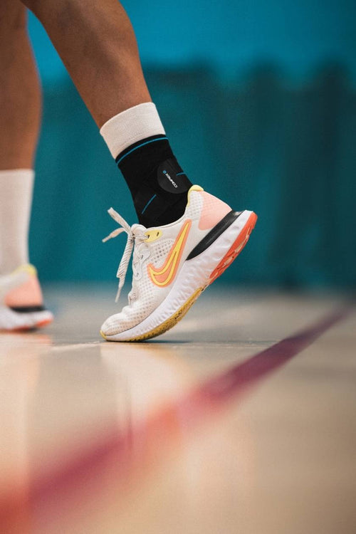 A man playing basketball, wearing the Compex Activ'® Ankle+ support