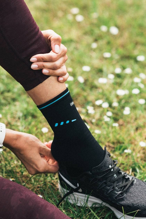 A woman putting a shoe on, wearing the Compex Activ’® Ankle Support