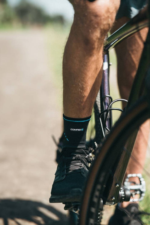 A man sitting on a mountain bike, wearing the Compex Activ’® Ankle Support