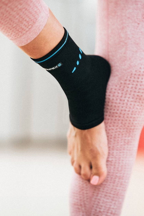 A woman doing yoga stretches, wearing the Compex Activ’® Ankle Support