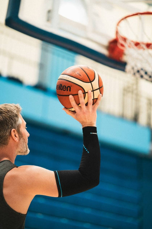 A man playing basketball, wearing the Compex Activ'® Arm Support Sleeves