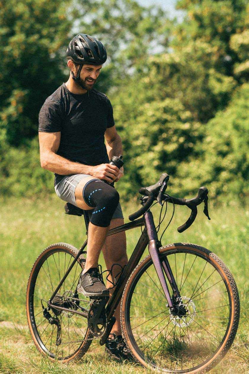 A man sitting on a mountain bike, wearing the Compex Activ’® Knee Support