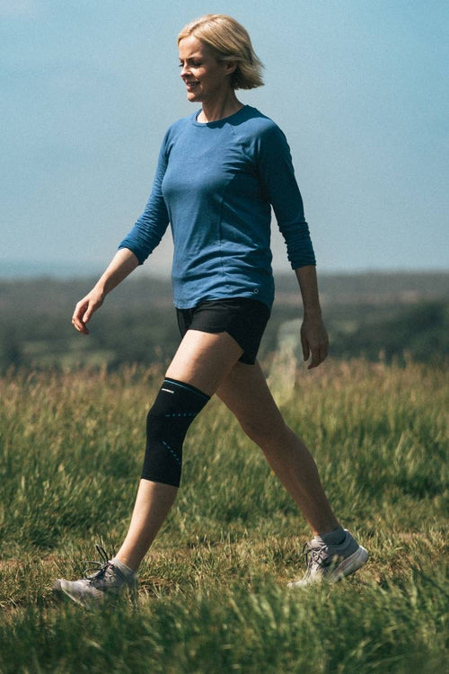 A woman walking through a field, wearing the Compex Activ’® Knee Support