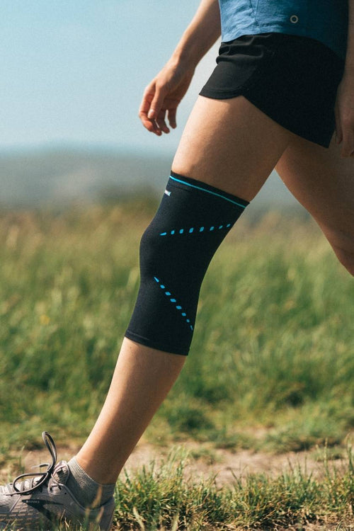 A woman walking through a field, wearing  the Compex Activ’® Knee Support