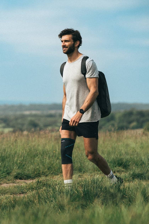A man walking through a field, wearing the Compex Activ’® Knee Support