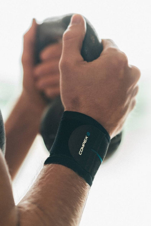 A man lifting a kettlebell, wearing the Compex Activ'® Wrist Band+ Support